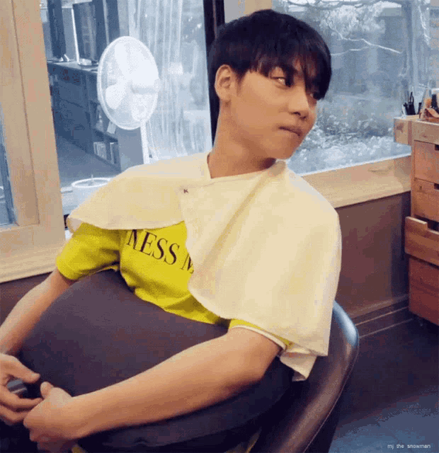 a man wearing a yellow shirt with the word mess on it sits in a chair