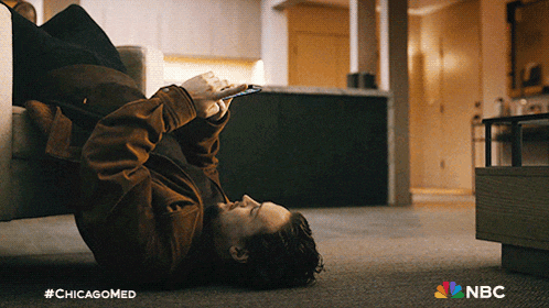 a man is laying on the floor looking at his phone with the nbc logo in the corner