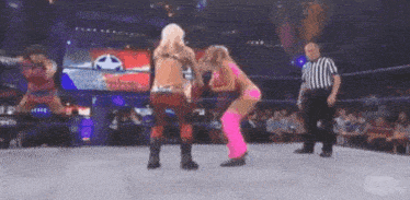 two women are wrestling in a ring with a referee in the background .