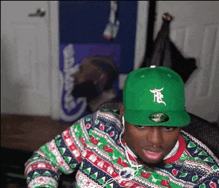 a man wearing a green hat and a christmas sweater is sitting at a desk .
