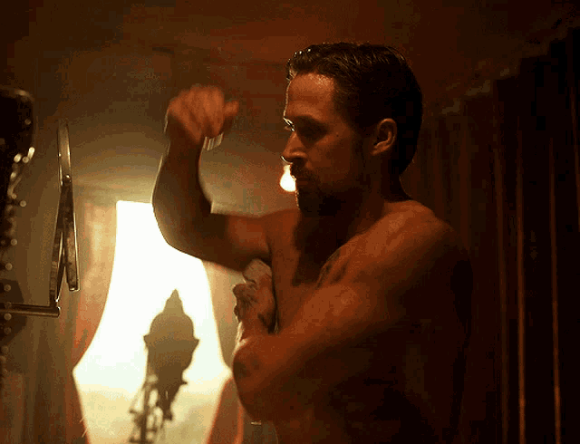 a shirtless man looks at himself in a mirror in a dark room