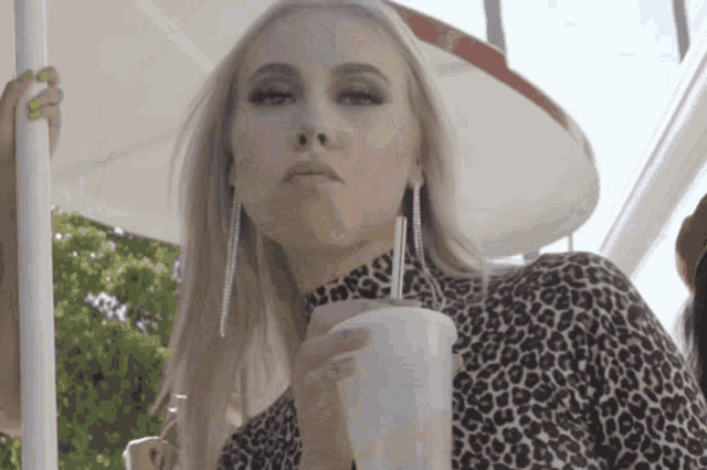 a woman in a leopard print top drinks from a plastic cup