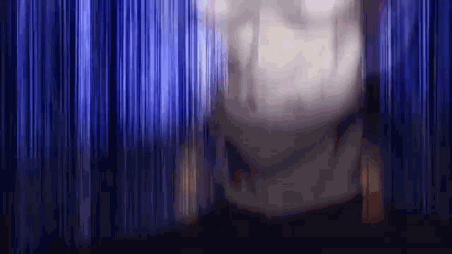 a blurred image of a person standing in front of a blue curtain