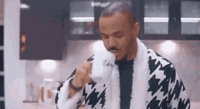 a man in a bathrobe is drinking from a cup in a kitchen .