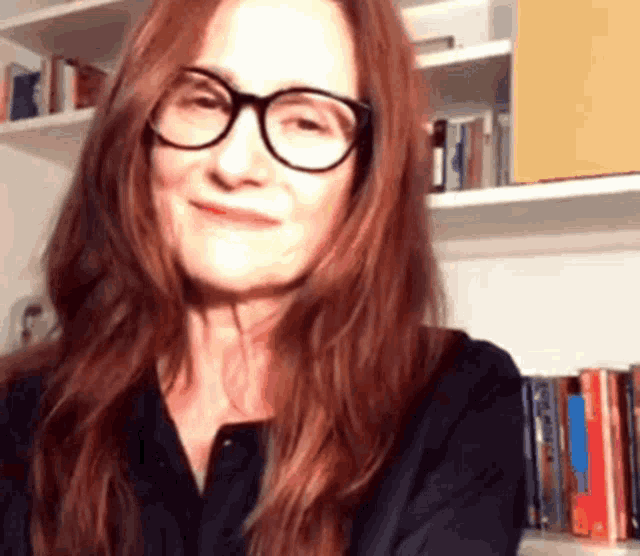 a woman wearing glasses and a black shirt is smiling in front of a bookshelf