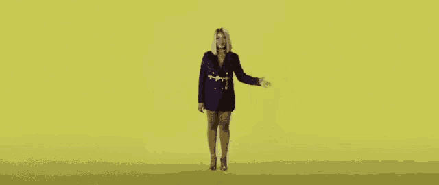 a woman in a blue dress and jacket is standing on a yellow background .