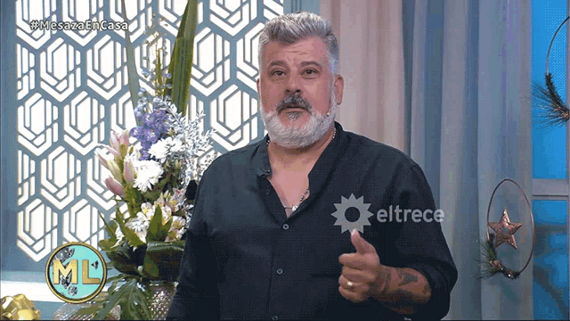 a man with a beard is giving a thumbs up in front of flowers and a sign that says eltrece