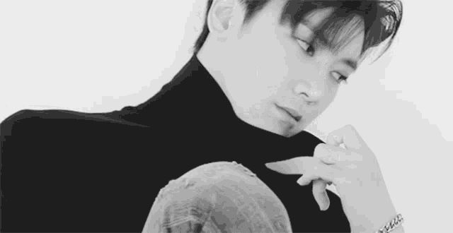 a black and white photo of a young man wearing a turtleneck sweater and a bracelet .