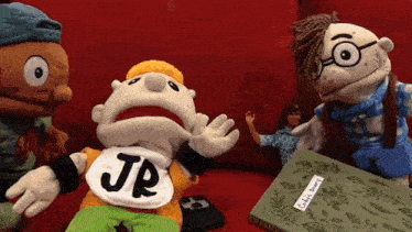 a puppet with jr on his shirt is standing next to a book