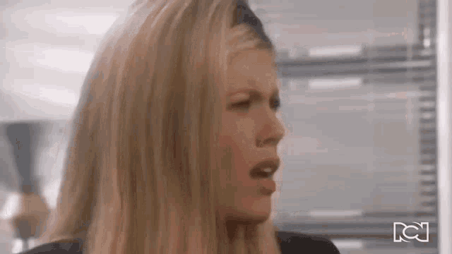 a woman with long blonde hair is making a funny face while standing in front of a window .