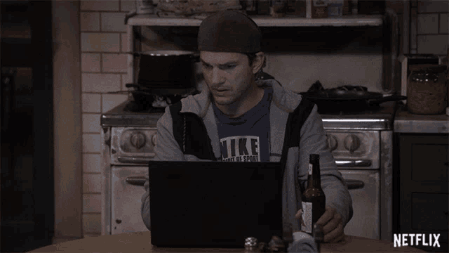 a man sitting at a table with a laptop and a bottle of beer with a netflix logo on the bottom right