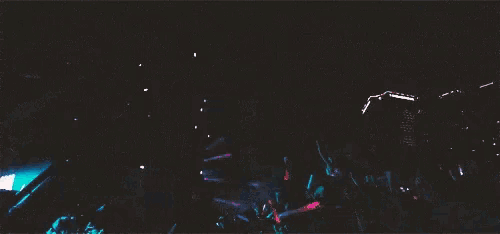 a crowd of people standing in front of a stage at a concert with smoke coming out of the stage .