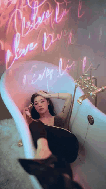 a woman is laying in a bathtub with a neon sign behind her that says love