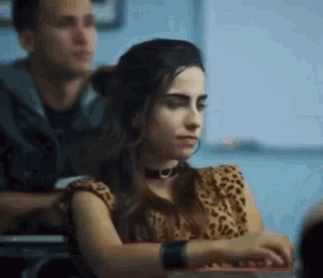 a woman wearing a choker is sitting at a desk in a classroom .
