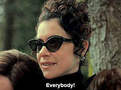a woman wearing sunglasses says " everybody " in front of a group of people