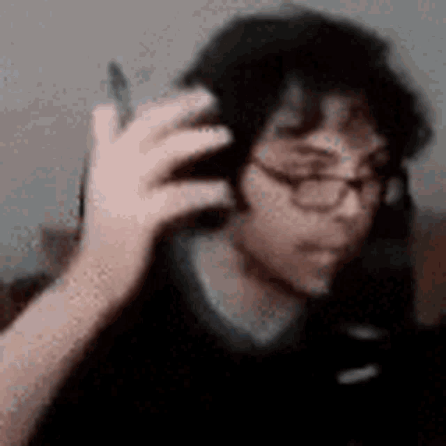 a blurry picture of a man wearing glasses and headphones holding a cell phone .