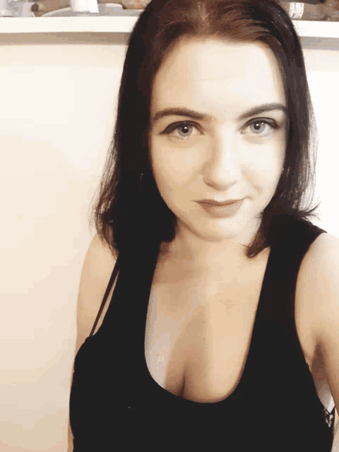 a woman wearing a black tank top with a plunging neckline looks at the camera