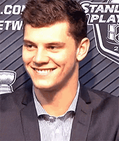 a man in a suit and striped shirt smiles in front of a stanley cup sign