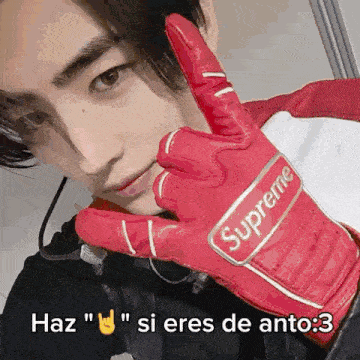 a man wearing a red supreme glove is giving the peace sign