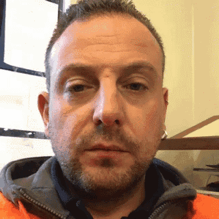 a man with a beard wearing an orange jacket is making a funny face .