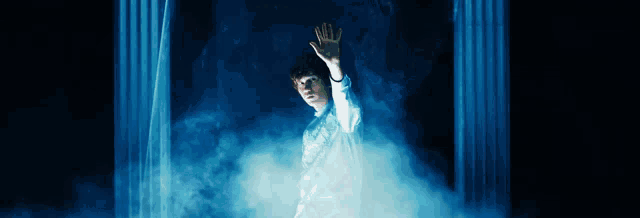 a man in a white shirt is standing in a dark room with his hand outstretched