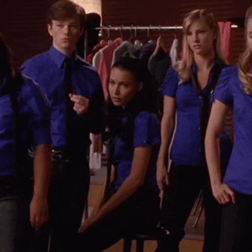a group of people wearing blue shirts and ties are standing in front of a rack of clothes