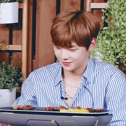 a young man in a striped shirt is sitting at a table with a tray of food on it .