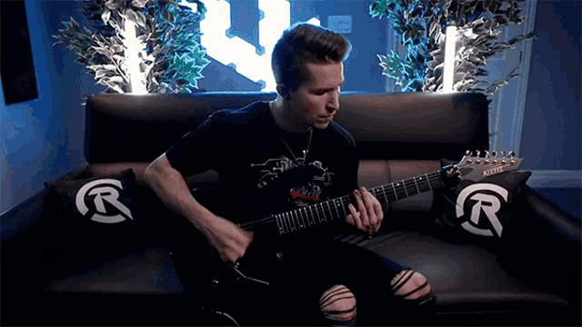 a man is playing a guitar on a couch with a r on the pillows