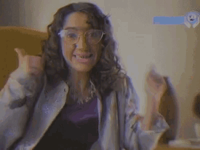 a woman with glasses giving a thumbs up in front of a wall that says peauf