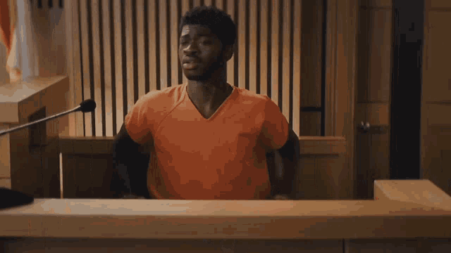 a man in an orange shirt is standing in front of a microphone in a courtroom