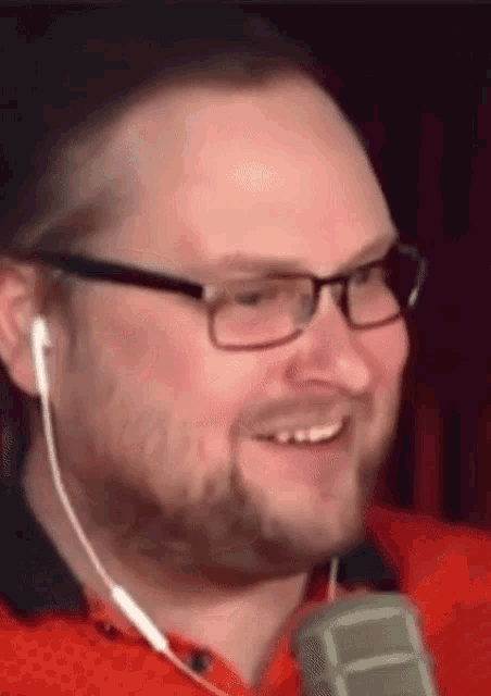 a man wearing glasses and earbuds is smiling while holding a microphone .