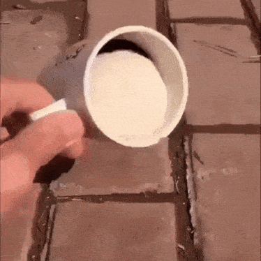 a person is pouring something into a plastic cup on a brick floor .
