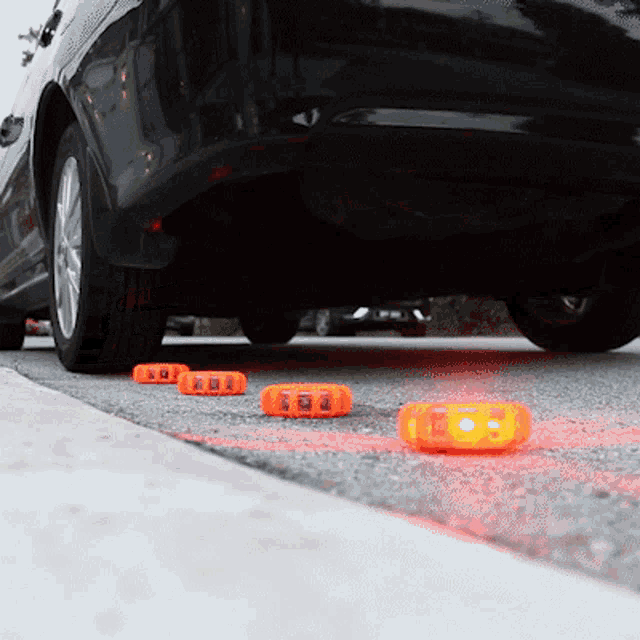 a black car is parked on the side of the road with orange lights on the ground
