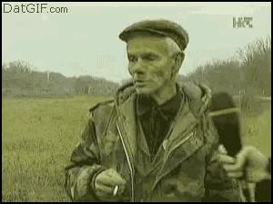 an old man is smoking a cigarette in a field while talking into a microphone .