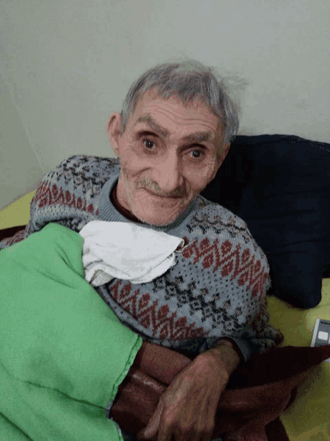 an elderly man in a sweater is laying in bed with a green blanket