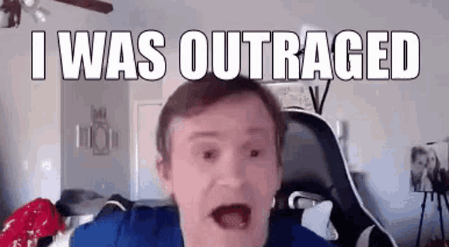 a man in a blue shirt is making a funny face while sitting in a chair in a room .