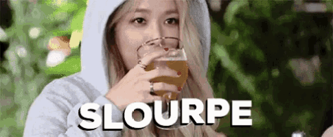 a woman in a hoodie is drinking a glass of beer and the word slourpe is on the bottom right
