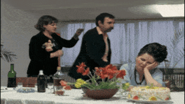 a woman is sitting at a table with a cake and a man standing behind her