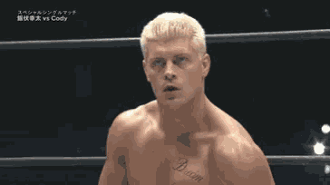 a man with blonde hair is standing in a boxing ring with his hands wrapped in bandages .
