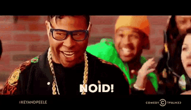 a man wearing glasses and a chain around his neck is laughing with a group of people .