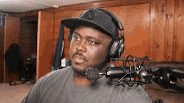 a man wearing headphones and a baseball cap is sitting in front of a microphone .