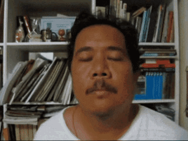 a man with his eyes closed in front of a bookshelf full of books