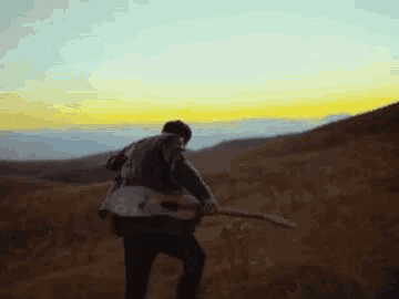 a man is playing a guitar in the desert at sunset .