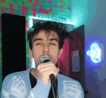 a young man is singing into a microphone in front of a sign that says kaykoluns