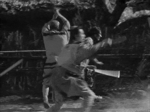 a black and white photo of a group of men fighting with swords