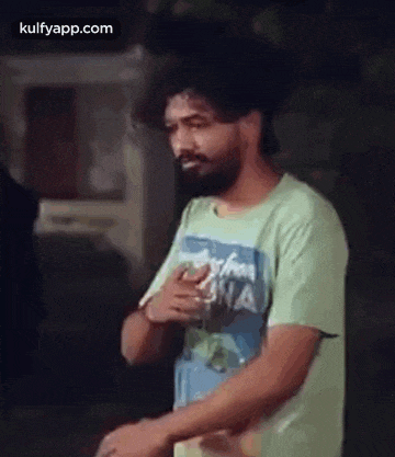 a man with a beard is wearing a green t-shirt and standing with his hands on his chest .