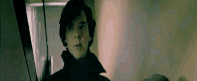 a man in a black coat is standing in a dark room looking at something .