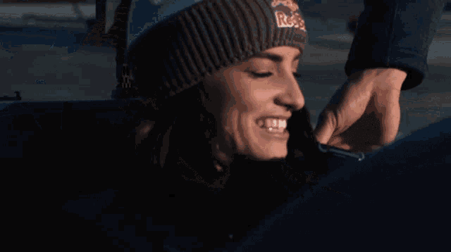 a woman wearing a red bull beanie laughs with her mouth open