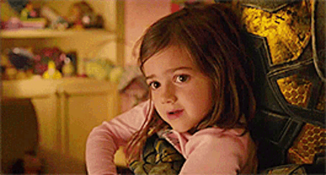 a little girl is sitting in a chair with a turtle blanket on her back .