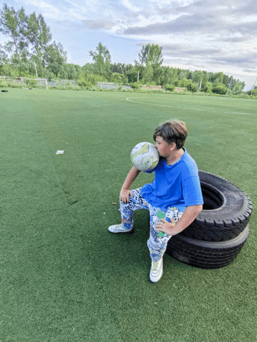 a boy sitting on a tire with a soccer ball on his face